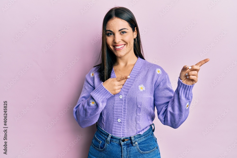 Young brunette woman wearing spring cardigan with flowers print smiling and looking at the camera pointing with two hands and fingers to the side. Young brunette woman wearing spring cardigan with flowers print smiling and looking at the camera pointing with two hands and fingers to the side.