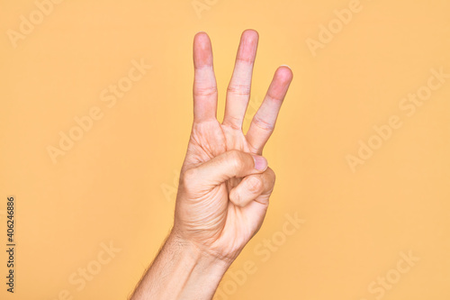 Hand of caucasian young man showing fingers over isolated yellow background counting number 3 showing three fingers