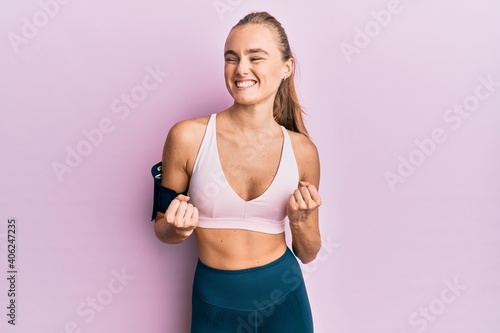 Beautiful blonde woman wearing sportswear and arm band excited for success with arms raised and eyes closed celebrating victory smiling. winner concept. © Krakenimages.com