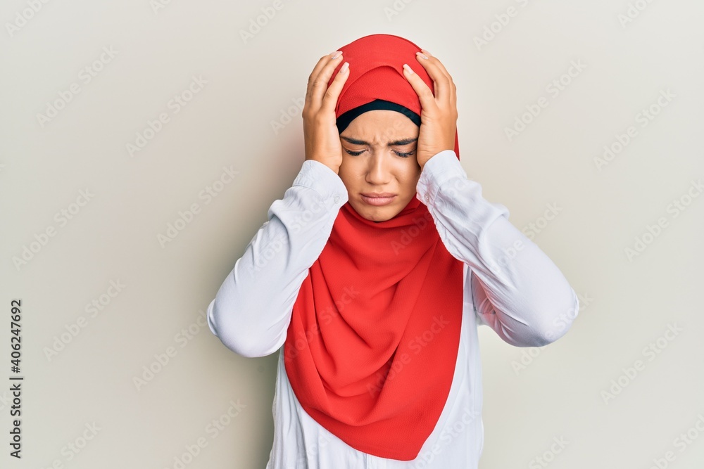 Young beautiful hispanic girl wearing traditional islamic hijab scarf suffering from headache desperate and stressed because pain and migraine. hands on head. Young beautiful hispanic girl wearing traditional islamic hijab scarf suffering from headache desperate and stressed because pain and migraine. hands on head.