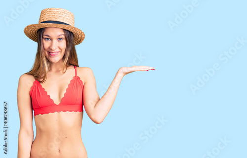 Beautiful brunette young woman wearing bikini smiling cheerful presenting and pointing with palm of hand looking at the camera.