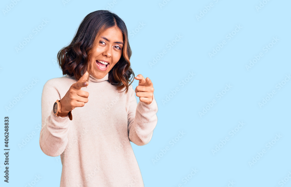 Young beautiful mixed race woman wearing winter turtleneck sweater pointing fingers to camera with happy and funny face. good energy and vibes.