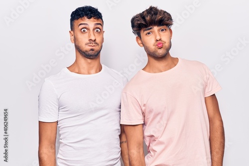 Young gay couple wearing casual clothes puffing cheeks with funny face. mouth inflated with air, crazy expression.