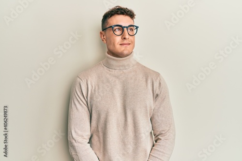 Hispanic young man wearing casual turtleneck sweater smiling looking to the side and staring away thinking.