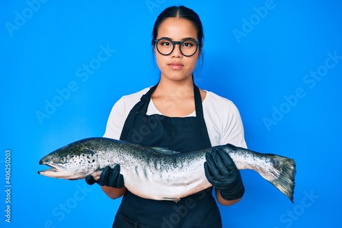 Young beautiful asian girl fishmonger selling fresh raw salmon relaxed with serious expression on face. simple and natural looking at the camera.