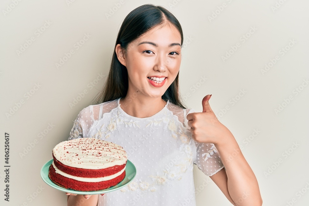 Young chinese woman holding carrot cake smiling happy and positive, thumb up doing excellent and approval sign Young chinese woman holding carrot cake smiling happy and positive, thumb up doing excellent and approval sign