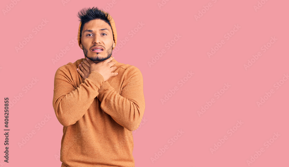 Fototapeta premium Handsome latin american young man wearing winter sweater and wool hat shouting and suffocate because painful strangle. health problem. asphyxiate and suicide concept.