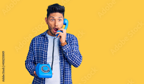 Handsome latin american young man holding vintage telephone scared and amazed with open mouth for surprise, disbelief face