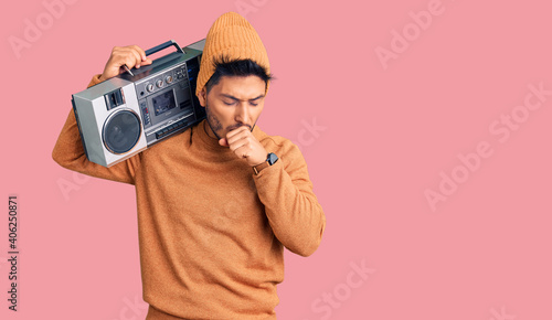 Handsome latin american young man holding boombox, listening to music feeling unwell and coughing as symptom for cold or bronchitis. health care concept.