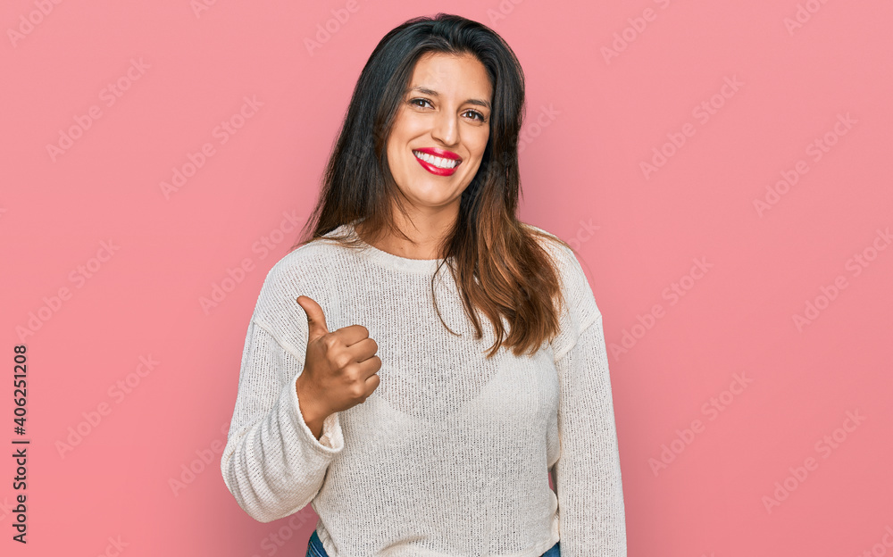 Beautiful hispanic woman wearing casual sweater doing happy thumbs up gesture with hand. approving expression looking at the camera showing success. Beautiful hispanic woman wearing casual sweater doing happy thumbs up gesture with hand. approving expression looking at the camera showing success.