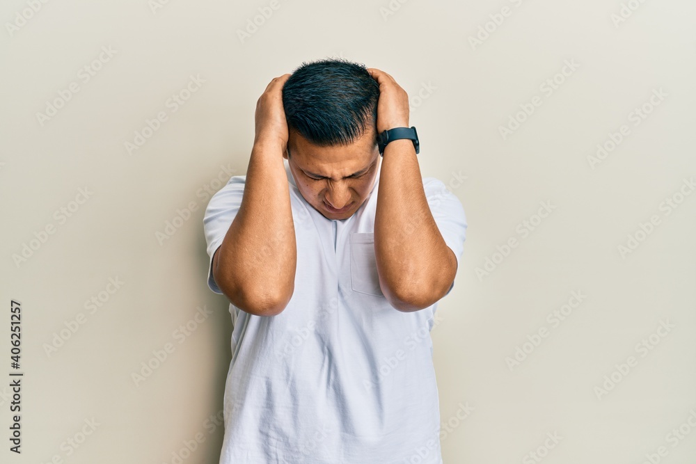 Young latin man wearing casual white t shirt suffering from headache desperate and stressed because pain and migraine. hands on head. Young latin man wearing casual white t shirt suffering from headache desperate and stressed because pain and migraine. hands on head.