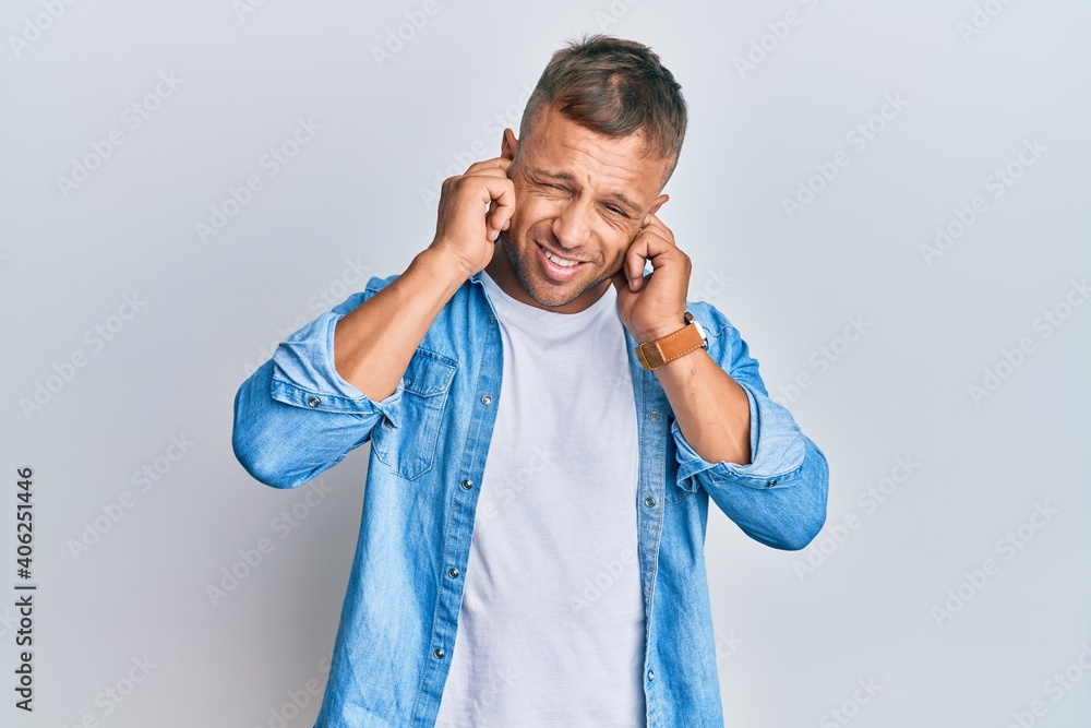 Handsome muscle man wearing casual denim jacket covering ears with fingers with annoyed expression for the noise of loud music. deaf concept. Handsome muscle man wearing casual denim jacket covering ears with fingers with annoyed expression for the noise of loud music. deaf concept.