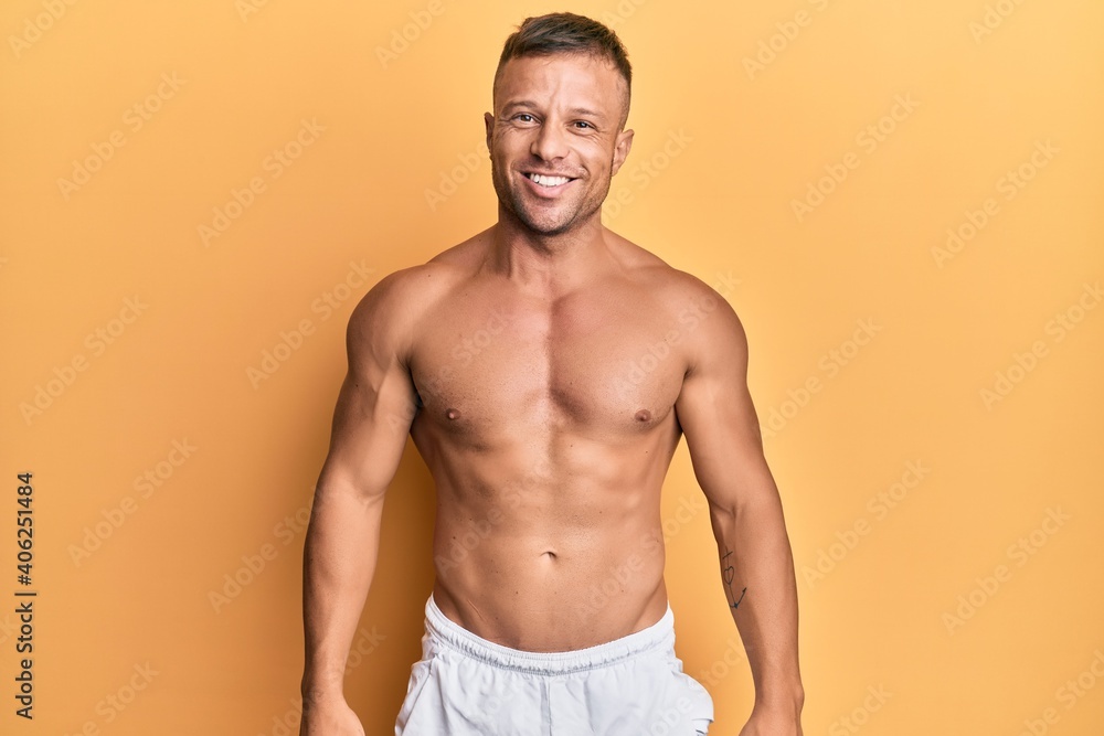 Handsome muscle man standing shirtless looking positive and happy standing and smiling with a confident smile showing teeth