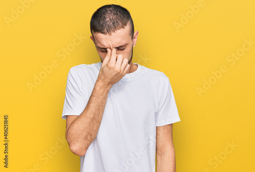 Hispanic young man wearing casual white t shirt tired rubbing nose and eyes feeling fatigue and headache. stress and frustration concept.