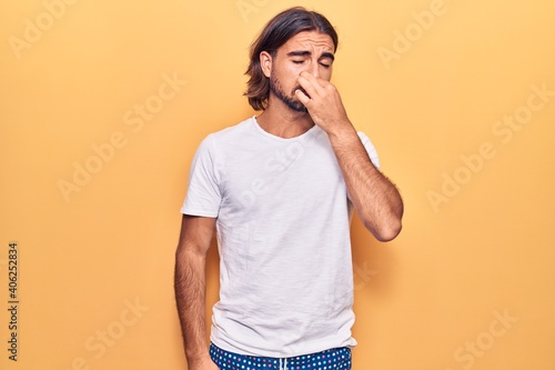 Young handsome man wearing casual clothes smelling something stinky and disgusting, intolerable smell, holding breath with fingers on nose. bad smell