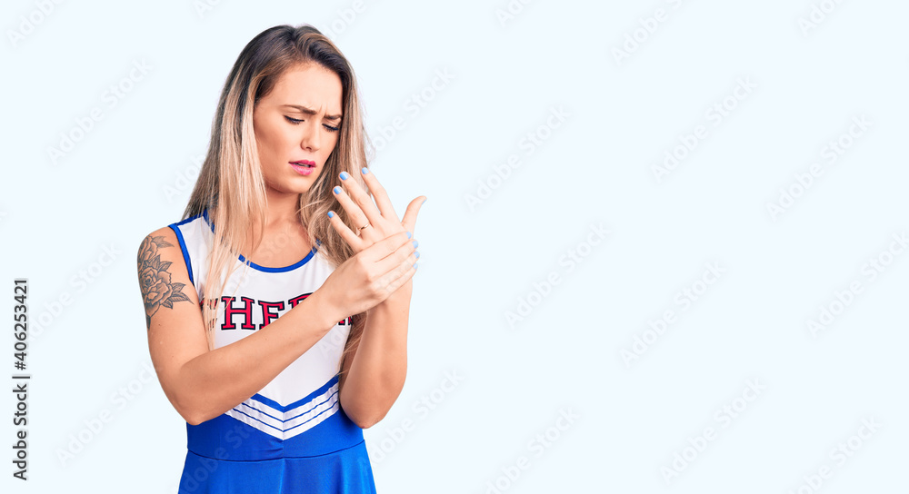 Young beautiful blonde woman wearing cheerleader uniform suffering pain on hands and fingers, arthritis inflammation Young beautiful blonde woman wearing cheerleader uniform suffering pain on hands and fingers, arthritis inflammation