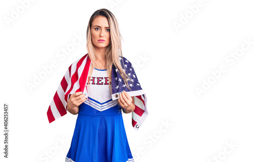 Young beautiful blonde woman wearing cheerleader uniform and united states flag thinking attitude and sober expression looking self confident