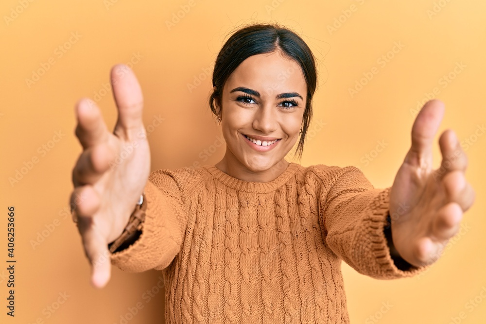 Young brunette woman wearing casual winter sweater looking at the camera smiling with open arms for hug. cheerful expression embracing happiness. Young brunette woman wearing casual winter sweater looking at the camera smiling with open arms for hug. cheerful expression embracing happiness.