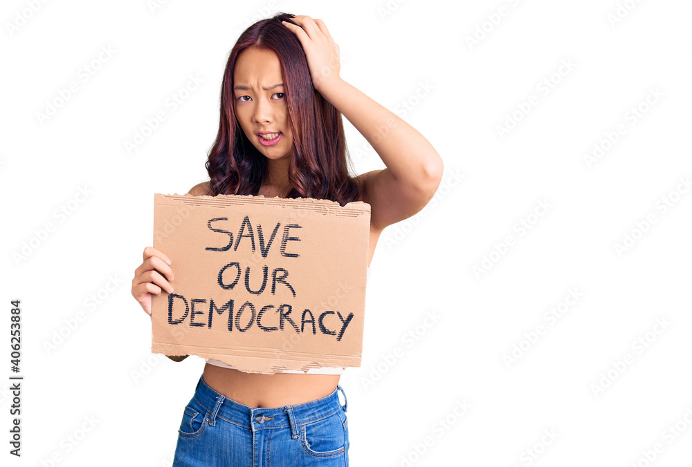 Young beautiful chinese girl holding save our democracy protest banner stressed and frustrated with hand on head, surprised and angry face Young beautiful chinese girl holding save our democracy protest banner stressed and frustrated with hand on head, surprised and angry face