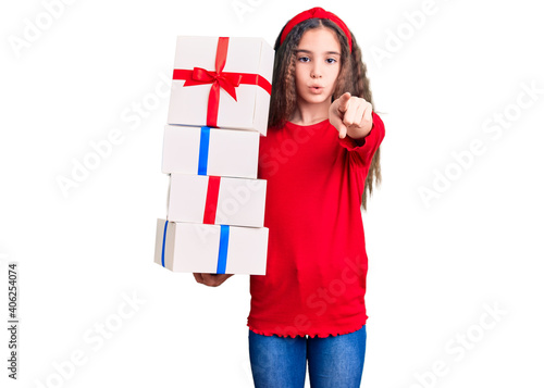 Cute hispanic child girl holding gift pointing with finger to the camera and to you, confident gesture looking serious