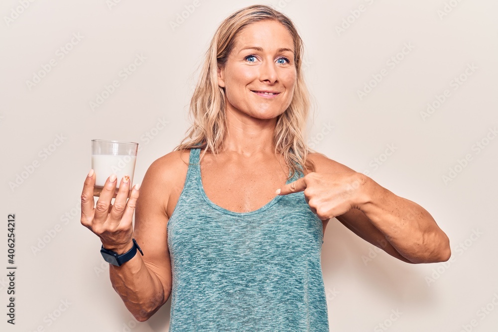 Middle age caucasian blonde woman holding a glass of milk pointing finger to one self smiling happy and proud Middle age caucasian blonde woman holding a glass of milk pointing finger to one self smiling happy and proud