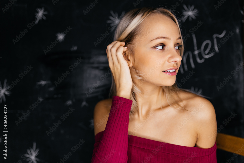 A young blonde girl with bare shoulders looks to the side. Portrait of a cutie on a dark background. High quality photo