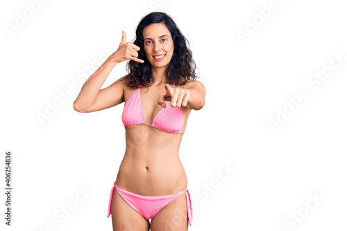 Young beautiful hispanic woman wearing bikini smiling doing talking on the telephone gesture and pointing to you. call me. © Krakenimages.com