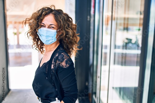 Middle age beautiful brunette woman wearing medical mask standing at terrace restaurant