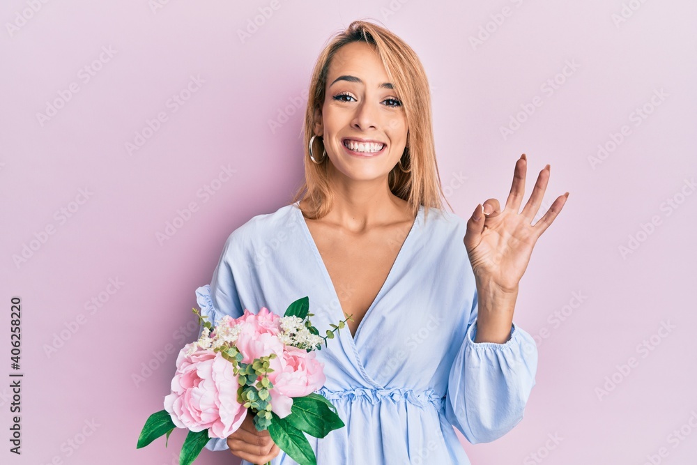 Beautiful blonde woman holding flowers doing ok sign with fingers, smiling friendly gesturing excellent symbol Beautiful blonde woman holding flowers doing ok sign with fingers, smiling friendly gesturing excellent symbol