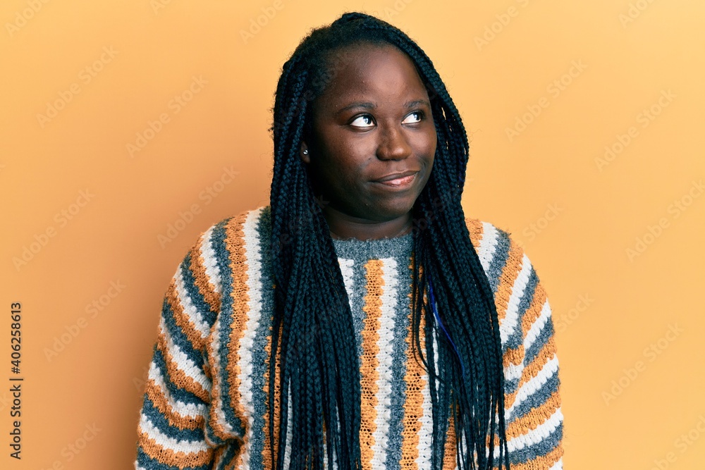Young black woman with braids wearing casual winter sweater smiling looking to the side and staring away thinking. Young black woman with braids wearing casual winter sweater smiling looking to the side and staring away thinking.