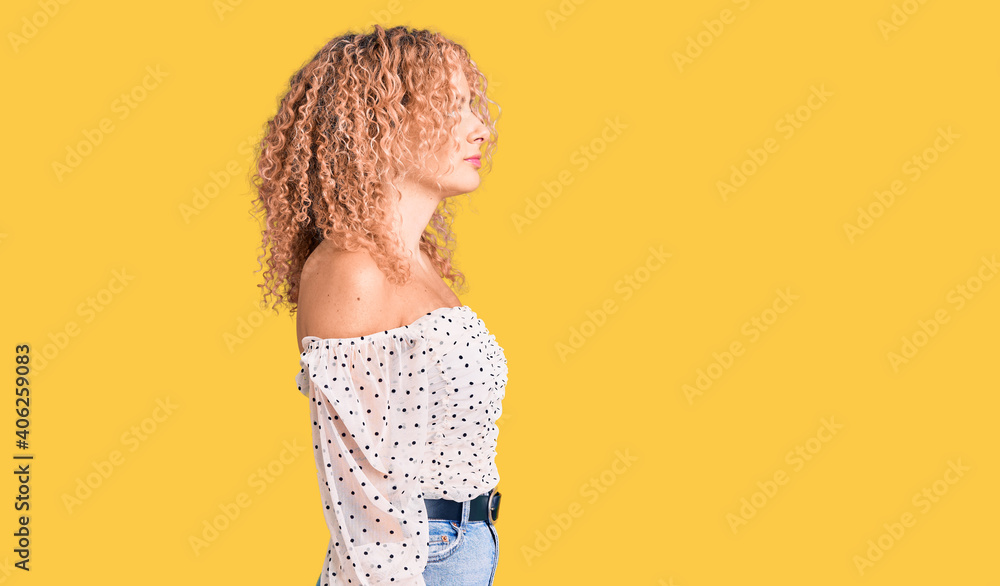 Young blonde woman with curly hair wearing casual clothes looking to side, relax profile pose with natural face with confident smile. Young blonde woman with curly hair wearing casual clothes looking to side, relax profile pose with natural face with confident smile.