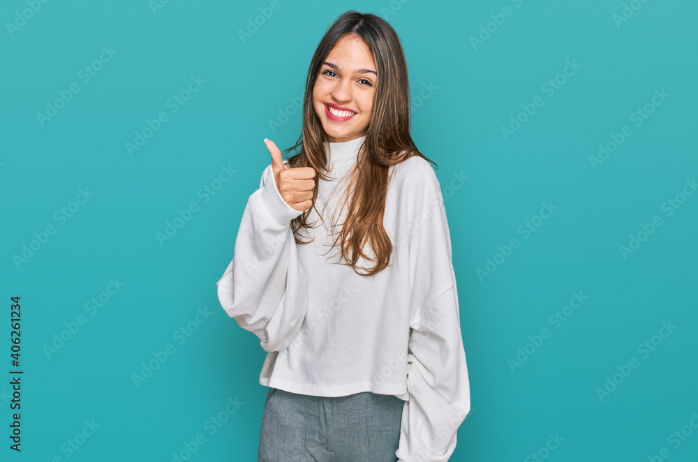 Young brunette woman wearing casual turtleneck sweater doing happy thumbs up gesture with hand. approving expression looking at the camera showing success. Young brunette woman wearing casual turtleneck sweater doing happy thumbs up gesture with hand. approving expression looking at the camera showing success.