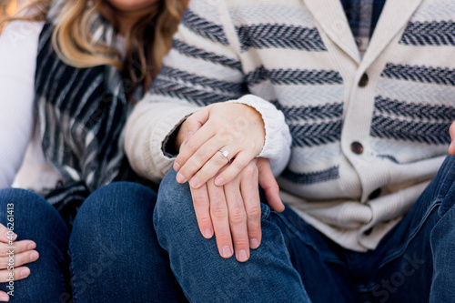 Couple sitting wearing blue jeans with hands resting on knee showing engagement ring. Faceless color horizontal photo. 