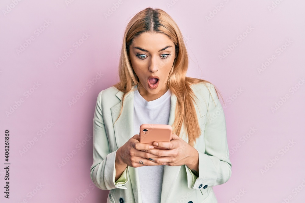 Young caucasian woman wearing business clothes using smartphone afraid and shocked with surprise and amazed expression, fear and excited face. Young caucasian woman wearing business clothes using smartphone afraid and shocked with surprise and amazed expression, fear and excited face.