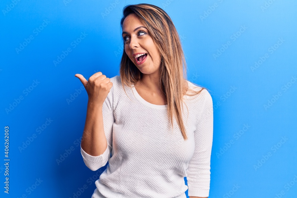 Young beautiful woman wearing casual t shirt pointing thumb up to the side smiling happy with open mouth Young beautiful woman wearing casual t shirt pointing thumb up to the side smiling happy with open mouth