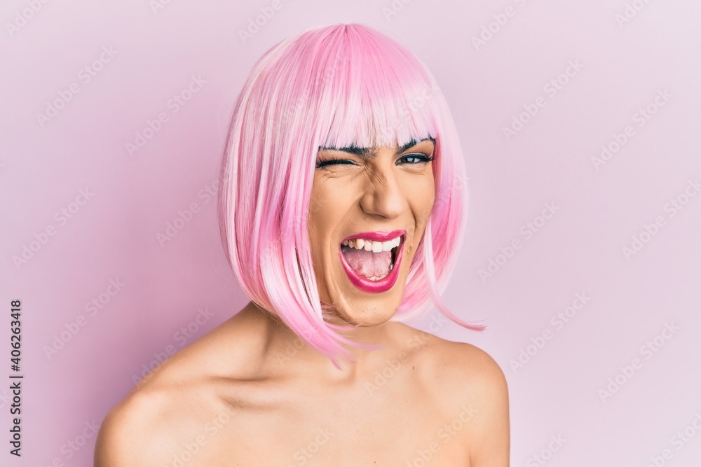 Young man wearing woman make up wearing pink wig winking looking at the camera with sexy expression, cheerful and happy face. Young man wearing woman make up wearing pink wig winking looking at the camera with sexy expression, cheerful and happy face.