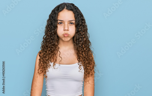 Teenager hispanic girl wearing casual clothes puffing cheeks with funny face. mouth inflated with air, crazy expression.