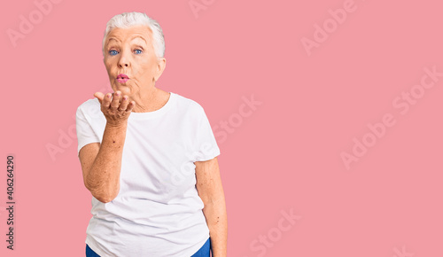Senior beautiful woman with blue eyes and grey hair wearing casual white tshirt looking at the camera blowing a kiss with hand on air being lovely and sexy. love expression.