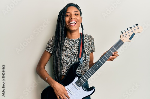 African american woman playing electric guitar smiling and laughing hard out loud because funny crazy joke. photo