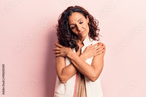 Middle age beautiful woman wearing casual vest hugging oneself happy and positive, smiling confident. self love and self care