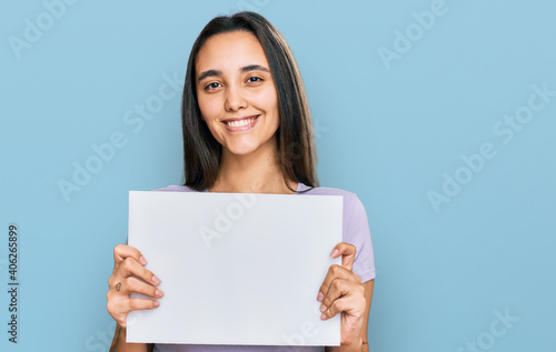 Young hispanic woman holding blank empty banner looking positive and happy standing and smiling with a confident smile showing teeth