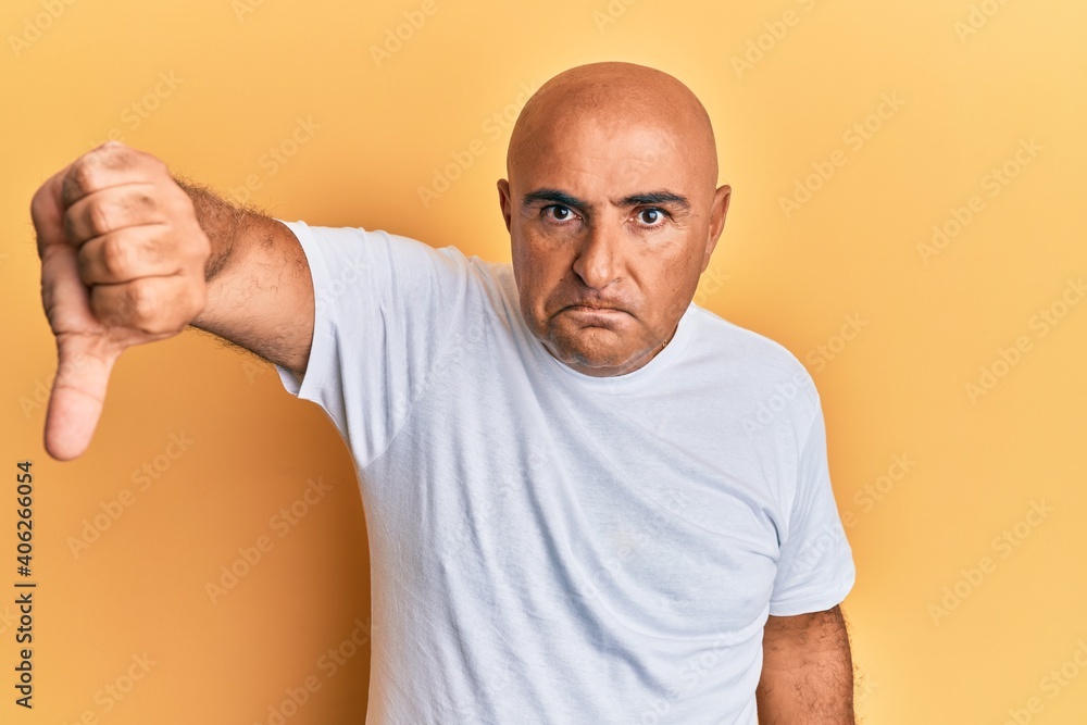 Mature middle east man wearing casual white tshirt looking unhappy and angry showing rejection and negative with thumbs down gesture. bad expression. Mature middle east man wearing casual white tshirt looking unhappy and angry showing rejection and negative with thumbs down gesture. bad expression.