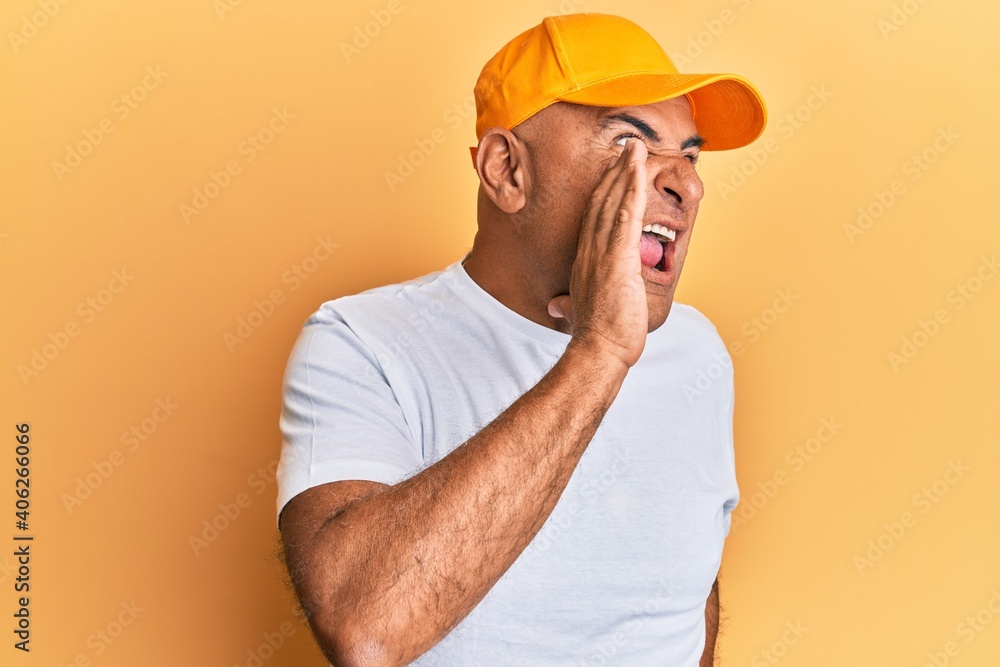 Mature middle east man with mustache wearing casual white tshirt and yellow cap shouting and screaming loud to side with hand on mouth. communication concept. Mature middle east man with mustache wearing casual white tshirt and yellow cap shouting and screaming loud to side with hand on mouth. communication concept.