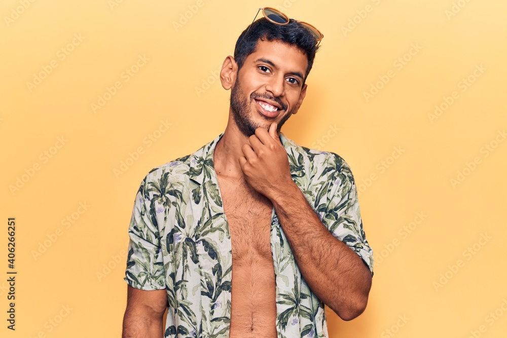 Young latin man wearing summer shirt and sunglasses smiling looking confident at the camera with crossed arms and hand on chin. thinking positive. Young latin man wearing summer shirt and sunglasses smiling looking confident at the camera with crossed arms and hand on chin. thinking positive.