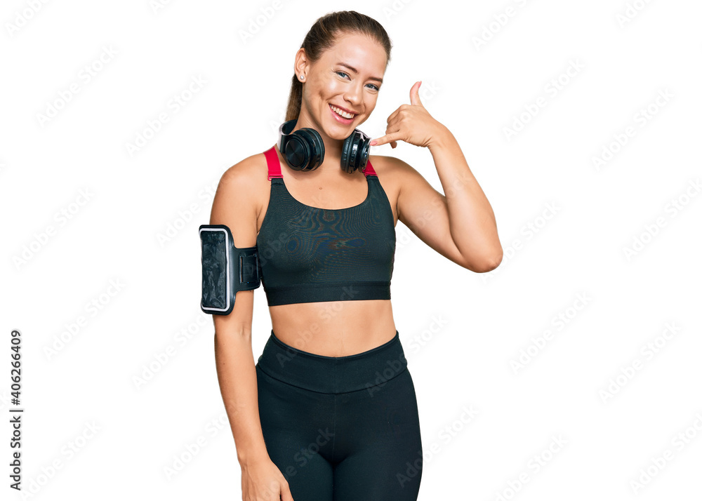Beautiful blonde woman wearing gym clothes and using headphones smiling doing phone gesture with hand and fingers like talking on the telephone. communicating concepts. Beautiful blonde woman wearing gym clothes and using headphones smiling doing phone gesture with hand and fingers like talking on the telephone. communicating concepts.