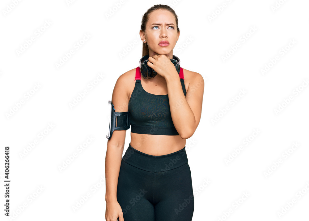 Beautiful blonde woman wearing gym clothes and using headphones touching painful neck, sore throat for flu, clod and infection Beautiful blonde woman wearing gym clothes and using headphones touching painful neck, sore throat for flu, clod and infection