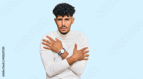 Young arab man wearing casual winter sweater shaking and freezing for winter cold with sad and shock expression on face