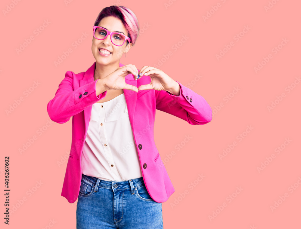 Young beautiful woman with pink hair wearing business jacket and glasses smiling in love showing heart symbol and shape with hands. romantic concept.