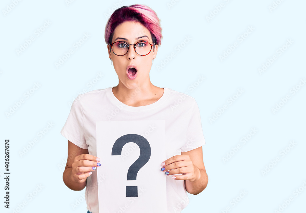 Young beautiful woman with pink hair holding question mark scared and amazed with open mouth for surprise, disbelief face Young beautiful woman with pink hair holding question mark scared and amazed with open mouth for surprise, disbelief face