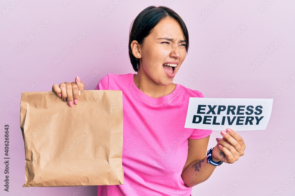 Beautiful young woman with short hair holding paper pag with express delivery text angry and mad screaming frustrated and furious, shouting with anger. rage and aggressive concept. Beautiful young woman with short hair holding paper pag with express delivery text angry and mad screaming frustrated and furious, shouting with anger. rage and aggressive concept.